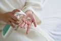 Young woman in a bathrobe press a bottle of body lotion onto her hand while sitting in bed. Close up Royalty Free Stock Photo