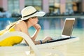 Young woman on beach chair at swimming pool working on computer laptop connected to wireless internet typing text on keys in
