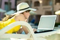 Young woman on beach chair at swimming pool working on computer laptop connected to wireless internet typing text on keys in