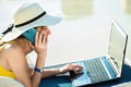 Young woman on beach chair at swimming pool working on computer laptop and talking on sell phone in summer resort. Remote work and Royalty Free Stock Photo