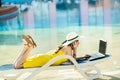 Young woman on beach chair at swimming pool working on computer laptop and talking on sell phone in summer resort. Remote work and Royalty Free Stock Photo