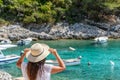 Young woman in beach clothes and sun hat looking at beautiful beach with boats and turquoise sea