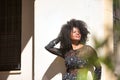 Young woman, beautiful and black with afro hair, with floral dress leaning on a wall, relaxed and quiet, seen through a green Royalty Free Stock Photo