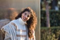 Young woman, beautiful, brunette with curly hair, sweater, coat and sunglasses, leaning against a metal wall, smiling and happy Royalty Free Stock Photo