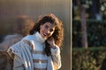 Young woman, beautiful, brunette with curly hair, sweater, coat and sunglasses, leaning against a metal wall, smiling and happy Royalty Free Stock Photo