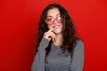 Young woman beautiful portrait, posing on red background, long curly hair, sunglasses in heart shape, glamour concept Royalty Free Stock Photo