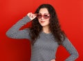 Young woman beautiful portrait, posing on red background, long curly hair, sunglasses in heart shape, glamour concept Royalty Free Stock Photo