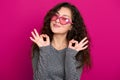 Young woman beautiful portrait show okay sign, posing on pink background, long curly hair, sunglasses in heart shape, glamour Royalty Free Stock Photo