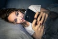 Young woman in bed holding a phone, tired and exhausted, blue light straining her eyes