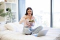 Young woman on bed at home and using modern laptop while eating healthy salad. Royalty Free Stock Photo