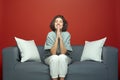 Young woman beg for dream, make praying gesture. Female imploring appealing, sitting on couch on red background Royalty Free Stock Photo
