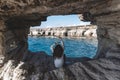 Young woman from behind is sitting in cave hole and looking at sea caves Royalty Free Stock Photo