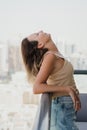 Young woman in beige crop top and blue denim shorts standing at the balcony and enjoying the weather