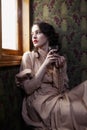 Young woman in beige vintage dress of early 20th century drinking tea in coupe of retro railway train