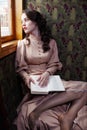 Young woman in beige vintage dress of early 20th century reading