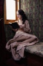 Young woman in beige vintage dress of early 20th century reading