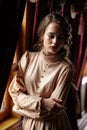 Young woman in beige vintage dress of early 20th century standing near window in corridor of retro railway train