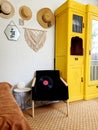 Young woman in beret sits in an armchair in cozy home, in room with music record in hands. Drinking wine. Vintage yellow cabinet