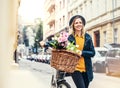 Young woman with bicycle and flowers in sunny spring town.
