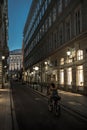 Woman On Bicycle In Narrow Road With Illuminated Stores In The Inner City Of Vienna In Austria