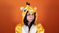 A young woman in a big pajamas of giraffe takes offence by something or someone on an orange background.