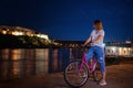 Young woman with a bike on the Novi Sad embankment overlooking the Petrovaradin fortress, night cityscape travel to Serbia, Balkan