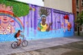 Young woman biking along colorful wall in Montevideo, Uruguay