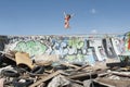 Young woman in bikini jumping over graffiti wall with garbage in foreground Royalty Free Stock Photo