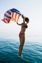 Young woman in bikini jumping in water with American flag Royalty Free Stock Photo