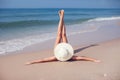 A young woman in bikini and in straw hat lying on a tropical beach, stretching up slender legs. Blue sea in the background. Royalty Free Stock Photo