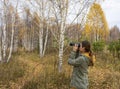 Young woman with binoculars watching birds in the autumn forest. Scientific research