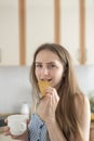 Young woman bites cracker and slyly looks at camera. Girl drinks coffee and eating cookies. Cheat meal. Vertical frame Royalty Free Stock Photo