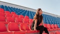 A young woman in black clothes with long hair is sitting on a stadium bleachers alone and and watching a sport game Royalty Free Stock Photo