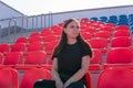 A young woman in black clothes with long hair is sitting on a stadium bleachers alone and and watching a sport game Royalty Free Stock Photo