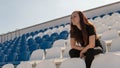 A young woman in black clothes with long hair is sitting on a stadium bleachers alone and and watching a sport game Royalty Free Stock Photo