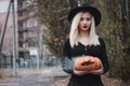 Young woman in the black coat holding the halloween pumpkin with the white smoke coming from inside of it in the autumn