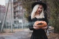 Young woman in the black coat holding the halloween pumpkin with the white smoke coming from inside of it in the autumn