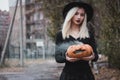 Young woman in the black coat holding the halloween pumpkin with the white smoke coming from inside of it in the autumn