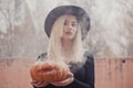 Young woman in the black coat holding the halloween pumpkin with the white smoke coming from inside of it in the autumn