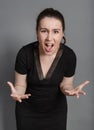 Young woman in a black dress is angry and screams against a gray background