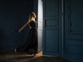 A young woman in a black dress opens a door from which light is pouring. Royalty Free Stock Photo