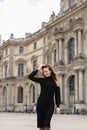 Young woman in black dress standing near Louvre with soft focus background, Paris.
