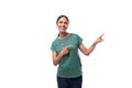 a young woman with black hair and a slender figure dressed in a green T-shirt attracts attention pointing with her hand Royalty Free Stock Photo