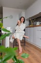 Young woman with black hair in white robe sits on chair the kitchen Royalty Free Stock Photo