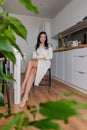 Young woman with black hair in white robe sits on chair the kitchen. Wellness and healthy food concept Royalty Free Stock Photo