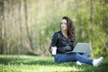 Young woman in a black jacked with coffee cup and laptop working outside in a park. Remote work. Digital work.