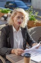 Young woman in a black jacket and glasses sitting at a table in street cafe, looking through documents. Business activity, Royalty Free Stock Photo