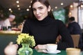 Young woman in black jersey look to camera, drink coffee and having rest in cafe near window. Royalty Free Stock Photo