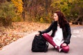 Young woman in leather jacket sitting in the middle of the road with a backpack on the background of autumn forest Royalty Free Stock Photo