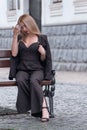 Young woman in black pantsuit rests on bench. Portrait of blonde girl in black outfit outdoor. Vertical frame